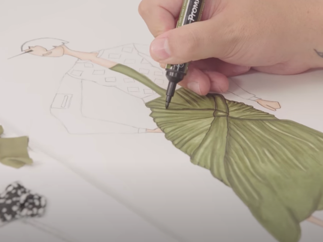 Someone coloring in green with a promarker the dress of a fashion sketch 