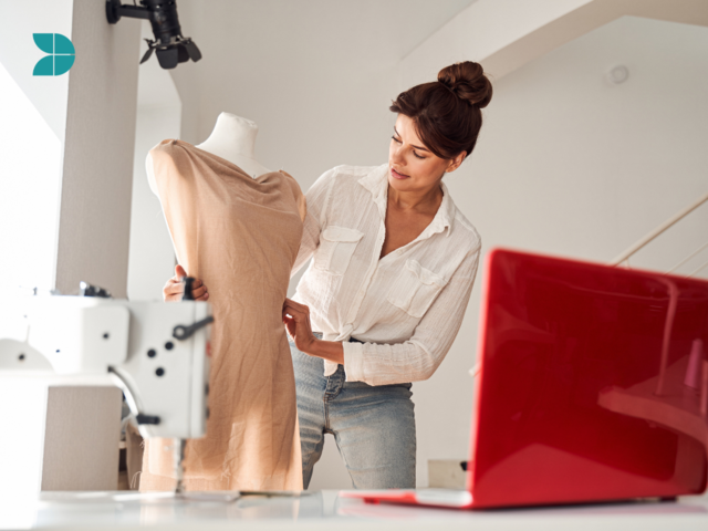 A fashion designer working with fabrics to create dress, a sewing machine and laptop in the desk.