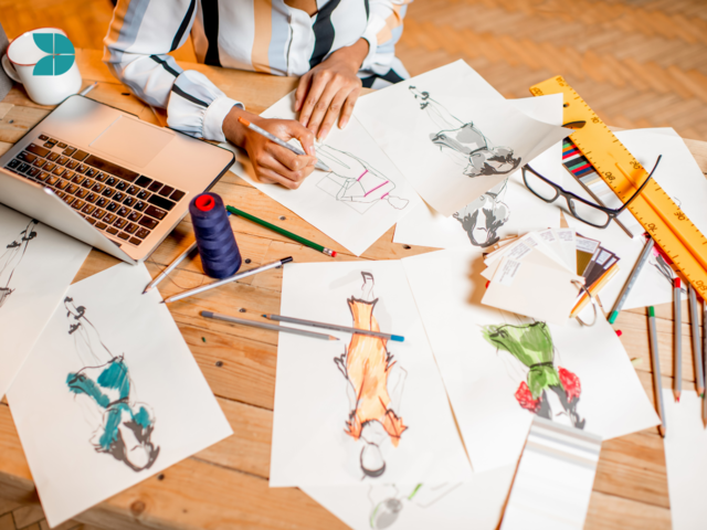A fashion designer working on several fashion design sketches on a desk.