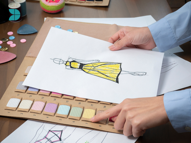 a person holding a sketch of a woman yellow dress choosing fabrics